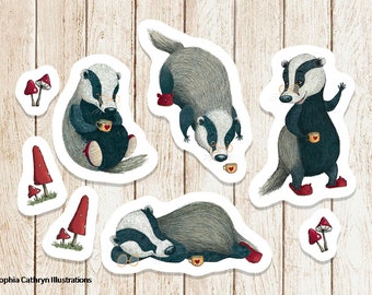 May include: Five illustrated stickers featuring a badger wearing glasses and holding a cup of tea. The badger is in different poses, including sitting, standing, and sleeping. There are also two stickers of red mushrooms.
