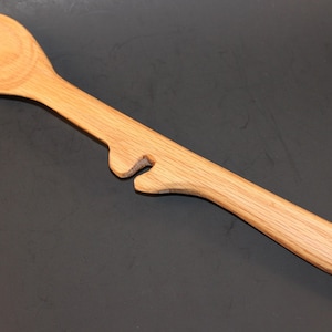 May include: A wooden spoon with a unique design featuring a cutout handle. The spoon is made of light brown wood and has a rounded bowl.