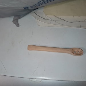 May include: A wooden spoon with two holes in the bowl. The spoon is light brown and has a smooth finish.
