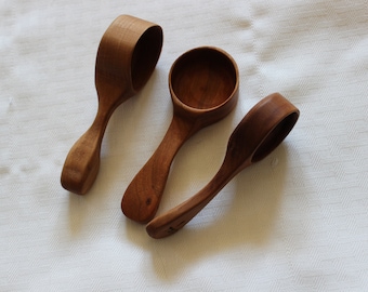 May include: Three wooden scoops of varying sizes, with rounded handles and a natural brown color. The scoops are arranged on a white surface.