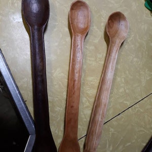 May include: Three wooden spoons of different colors and sizes. The spoons are made of dark wood, light wood, and a reddish brown wood. The spoons are all long and slender with rounded bowls.