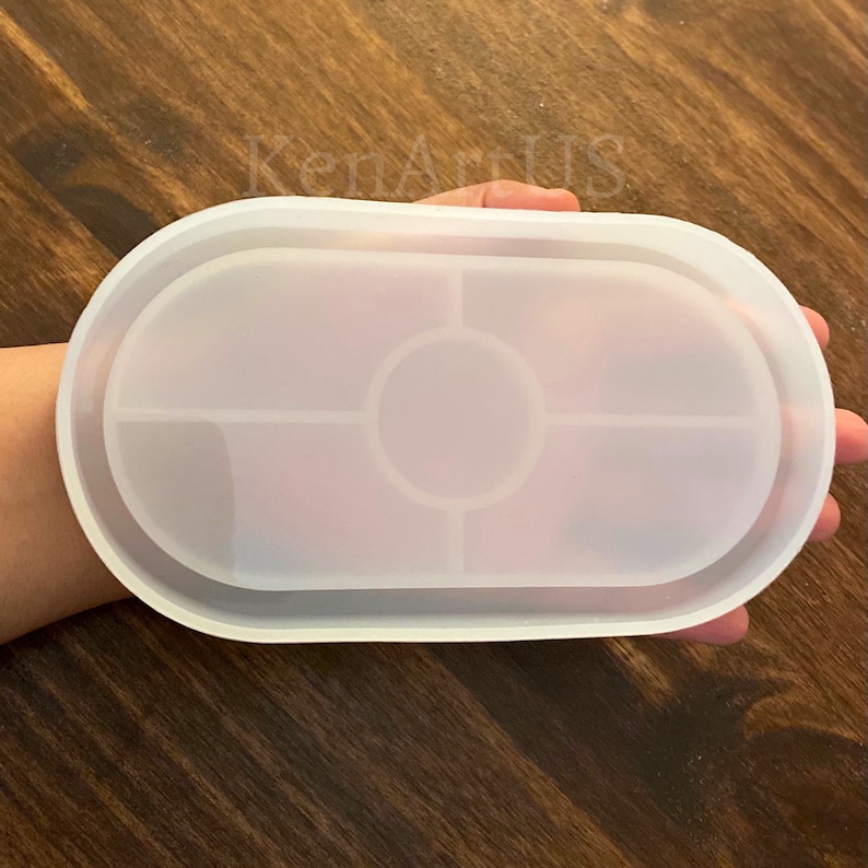 Puede incluir: Molde de silicona blanco para fundici&oacute;n de resina. El molde tiene forma ovalada con un borde elevado y una secci&oacute;n central circular dividida en cuatro secciones.