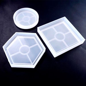 May include: Three silicone molds for making coasters. The molds are in the shapes of a circle, a square, and a hexagon. Each mold has a center circle and four smaller circles around it.