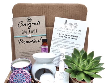 May include: A gift box with a succulent plant, a white ceramic oil diffuser, two candles, a bottle of essential oil, a turquoise bracelet with a silver charm, and a card that says "Congrats on your promotion!"