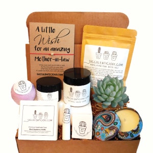 Op de afbeelding: Een cadeaudoos gevuld met bad- en lichaamsverzorgingsproducten, waaronder een badbom, een suikerscrub, zeep, lippenbalsem, badzout en een kaars. De doos bevat ook een kleine succulent plant en een kaart met de tekst "Een kleine wens voor een geweldige schoonmoeder".