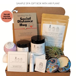 Op de afbeelding: Een bruine kartonnen cadeaudoos gevuld met spa-artikelen, waaronder badzout, een suikerscrub, zeep, een lippenbalsem, een kaars en een luchtplant. De doos heeft een kaart met de tekst "Sending You A... Social Distance Hug".