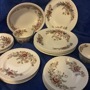 May include: A set of vintage floral patterned ceramic dinnerware, including plates, bowls, and a soup bowl. The plates and bowls have a white background with a brown, green, and pink floral design.