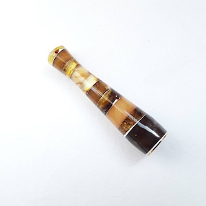 May include: A brown and amber cigarette holder with a striped pattern. The holder is made of multiple pieces of amber that have been glued together.