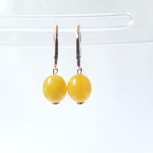 May include: A pair of leverback earrings with bright yellow, spherical beads. The earrings have silver-coloured metal components and are displayed against a white background. The round beads are a vibrant, sunny yellow colour.