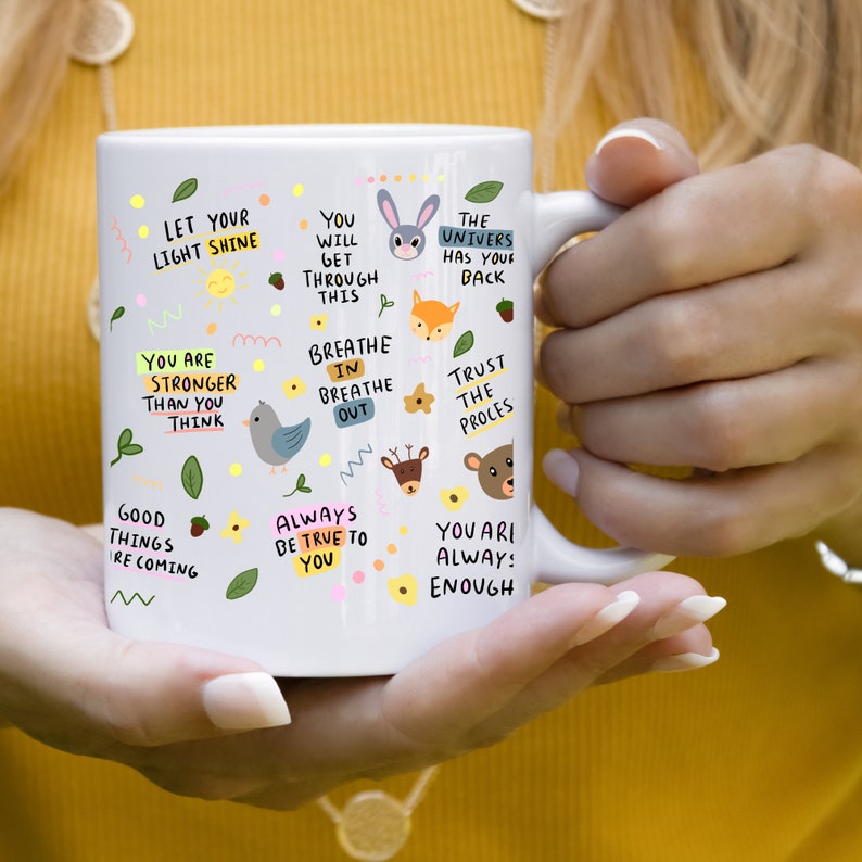 May include: White ceramic mug with inspirational quotes and illustrations of animals. The quotes include "Let your light shine", "You are stronger than you think", "You will get through this", "Breathe in breathe out", "The universe has your back", "Trust the process", "Good things are coming", "Always be true to you", and "You are always enough".