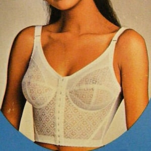 Può includere: Un indumento intimo di pizzo bianco con chiusura a cerniera frontale. L'indumento intimo ha un corpetto aderente e spalline regolabili.