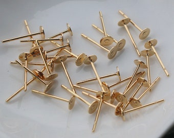 May include: A pile of gold-colored earring posts with flat round backs. The posts are about 1 inch long.