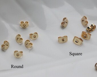 May include: A close-up of two sets of earring backs. The set on the left has round backs, and the set on the right has square backs. Both sets are gold-colored.