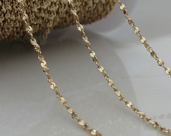 May include: Close-up of a delicate gold-colored chain. The chain is composed of small, flat, circular links connected in a repeating pattern. The chain is displayed against a neutral background, highlighting its intricate design. Ideal for jewelry making.