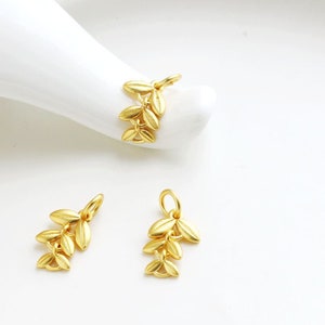 Może przedstawiać: Trzy złote zawieszki w kształcie liści, każda z inną liczbą liści. Zawieszki idealnie nadają się do dodania elegancji projektom biżuterii.