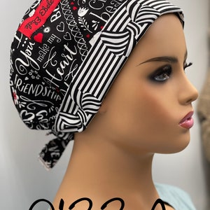 May include: Black and white patterned surgical scrub hat with the text "You make my heart" and "Friendship" in white lettering. The hat has a red label with the text "Ebele" in white lettering. The hat is on a mannequin wearing a light blue scrub top. The text "0133 A" is written below the mannequin.