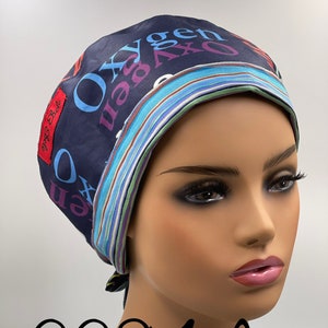 May include: A blue and white striped surgical scrub cap with the word "Oxygen" printed in various colors. The cap has a tie at the back and the text "Gigi Bella" is printed on the side.