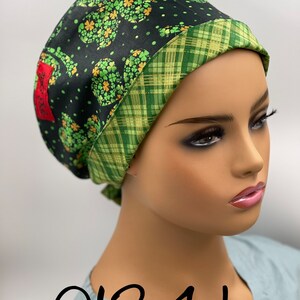 Puede incluir: Un gorro de quir&oacute;fano negro y verde con estampado de tr&eacute;bol y ribete de cuadros verde y dorado. El gorro tiene una etiqueta con el texto "0134 L".