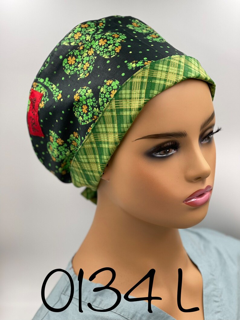 Puede incluir: Un gorro de quir&oacute;fano negro y verde con estampado de tr&eacute;bol y ribete de cuadros verde y dorado. El gorro tiene una etiqueta con el texto "0134 L".