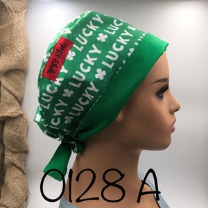 May include: Green surgical scrub hat with a white print of the word "lucky" and shamrocks. The hat has a green tie. The text "0128 A" is written in black below the hat.