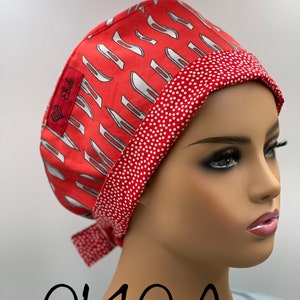 May include: Red and white surgical scrub hat with a white knife pattern and white polka dots. The hat has a label that says "Ebele". The hat is tied at the back. The text "0140 A" is written below the hat.