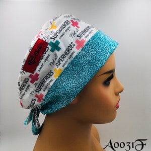 May include: A white scrub hat with a turquoise trim and a colourful pattern featuring the text "Not all superheroes wear capes." The hat has a red heart with the word "Ebele" on it.