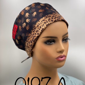 May include: A black scrub hat with a leopard print trim and a pattern of multi-colored hands. The hat has a tie at the back. The hat is on a mannequin's head. The text "0197 A" is visible in the image.
