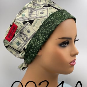 May include: A green and white scrub hat with a money print design. The hat has a green satin trim with a leafy pattern. The hat is tied with a green and white string. The hat is labeled "0034A".