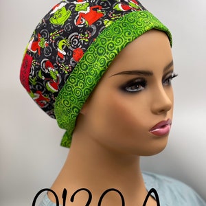 May include: A green and black scrub hat with a Grinch print and a green swirl pattern on the trim. The hat is tied with a green tie. The text "0120 A" is printed on the front of the hat.
