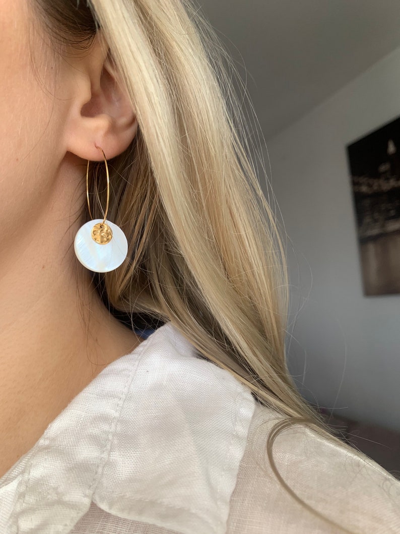 May include: Gold hoop earrings with a white shell pendant. The shell has a textured surface and a gold accent.