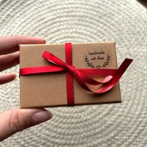 May include: A small brown box tied with a red ribbon. The box has a sticker that says "handmade with love" and a small heart.