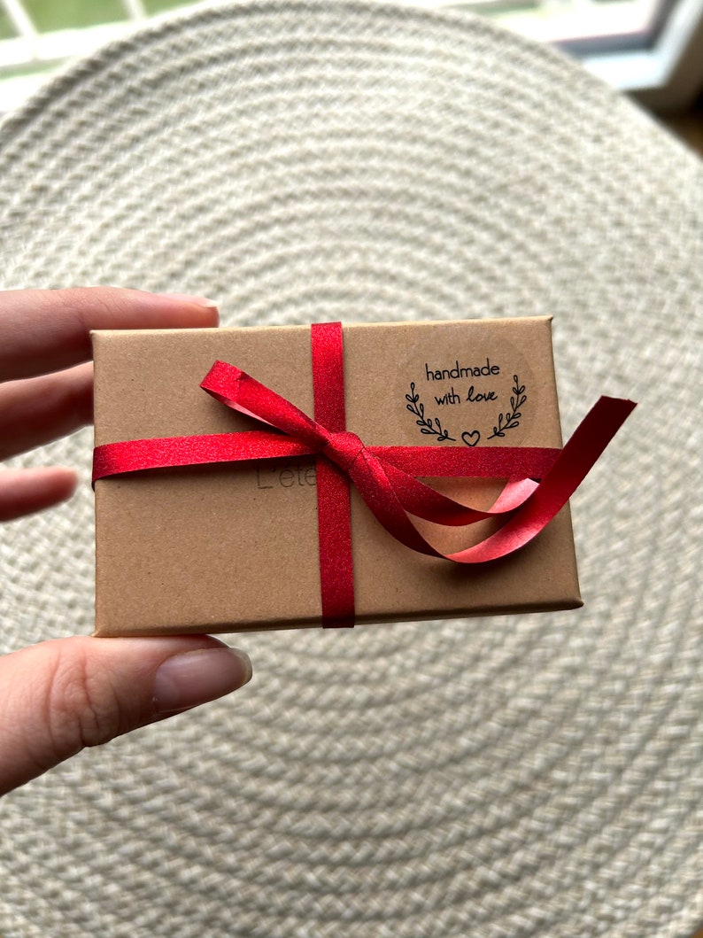 May include: A small brown box tied with a red ribbon. The box has a sticker that says "handmade with love" and a small heart.