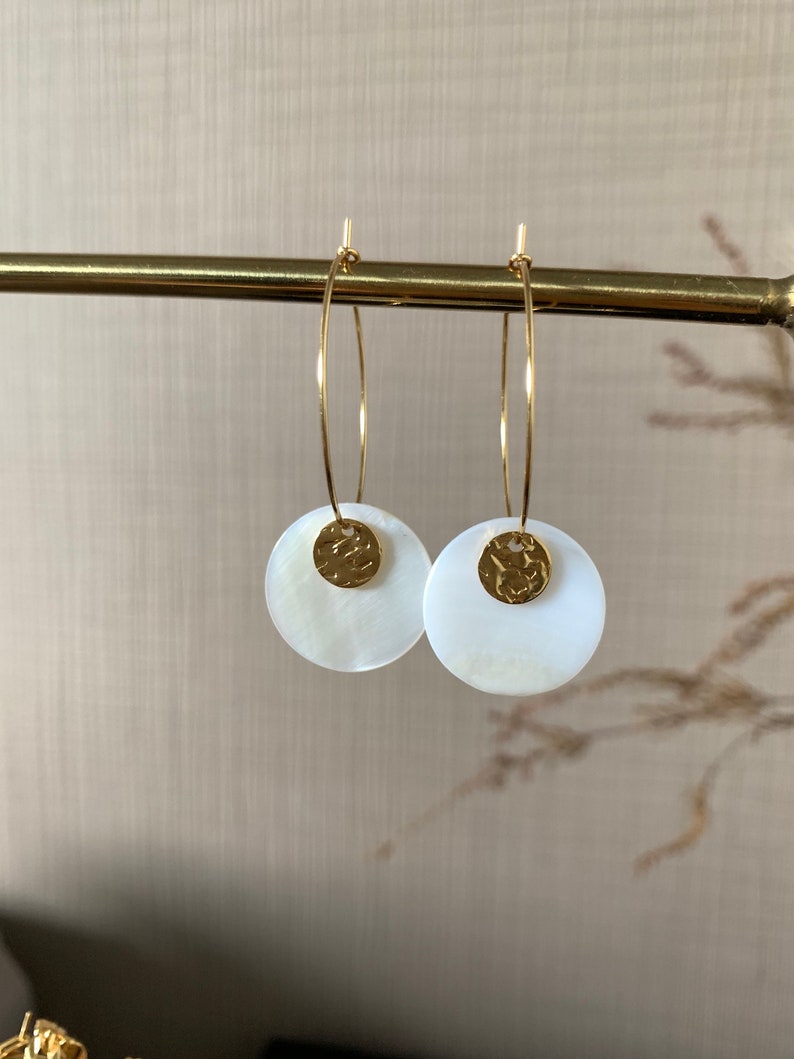 May include: A pair of gold hoop earrings with white shell and gold disc accents.