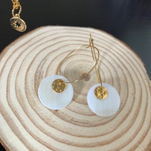 May include: Gold hoop earrings with white shell accents. The shell is textured and has a gold disc in the center.
