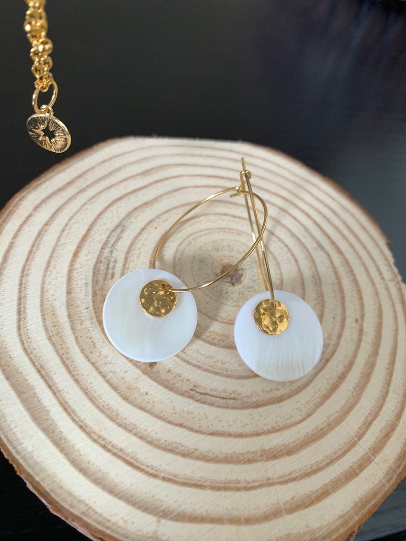 May include: Gold hoop earrings with white shell accents. The shell is textured and has a gold disc in the center.