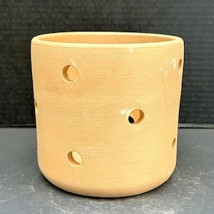May include: A terracotta planter with drainage holes. The planter is a light brown color and has a cylindrical shape.