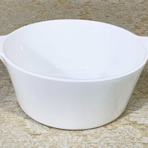 May include: A white ceramic baking dish with two handles. The dish is empty and has a smooth, glossy finish.