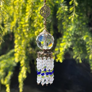 May include: A crystal suncatcher with a clear glass orb and a beaded tassel. The tassel is made of clear, green, and blue beads.