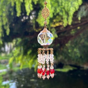 May include: A crystal suncatcher with a faceted glass ball, a gold filigree charm, and red and clear crystal beads hanging from a gold chain.