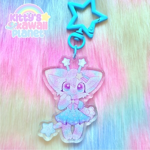 May include: A clear acrylic charm featuring a cute cartoon character with large eyes, a dress, and star accents. The charm is attached to a blue star-shaped clasp. The text "kitty's kawaii planet" is in the upper left corner.