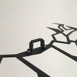 May include: Black metal wall decor with a geometric design. The decor has a hanging hook on the back.