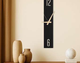 Puede incluir: Un reloj de pared negro rectangular moderno con números plateados que indican 12 y 6. Las manecillas del reloj son de color beige claro. El reloj está montado en una pared beige, con jarrones decorativos y una escultura sobre una superficie de madera.