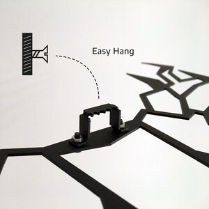 May include: Close-up of a black metal wall art piece with a geometric design. The image shows the mounting hardware, including a bracket and screws, with the text "Easy Hang" indicating ease of installation.