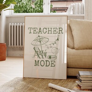 May include: A framed poster with the words "TEACHER MODE" in green, featuring an illustration of a beach scene. The poster is leaning against a beige sofa in a bright room with a large window and a wooden chair.