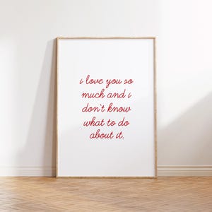 May include: A framed print with the words "i love you so much and i don't know what to do about it" in red script. The print is in a light wood frame and is displayed against a white wall.