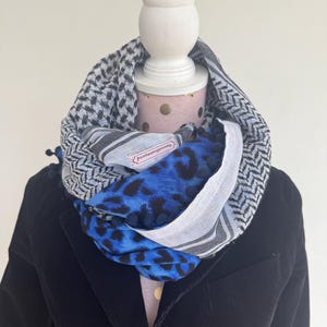 Könnte beinhalten: Ein schwarz-weiß-blauer gemusterter Schal mit einem blauen Leopardenmuster. Der Schal ist um einen weißen Mannequin-Kopf gebunden. Der Schal hat ein kleines Etikett mit der Aufschrift "AccessoriesbyJenny".