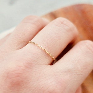 K&ouml;nnte beinhalten: Ein zarter goldener Kettenring an einem Finger.