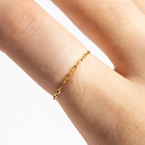 K&ouml;nnte beinhalten: Ein zarter goldener Kettenring, der an einem Finger getragen wird.