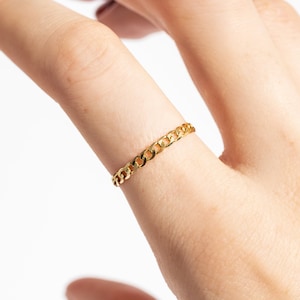 May include: A gold chain ring on a finger.