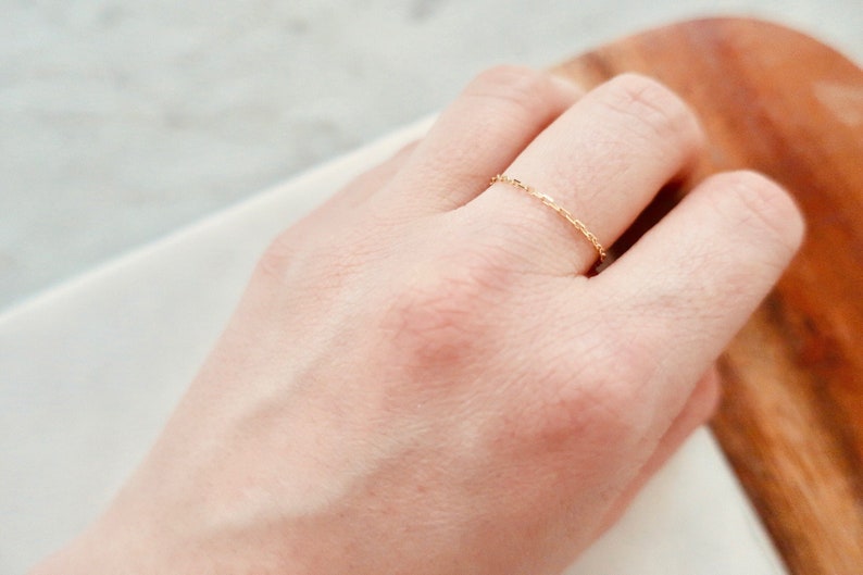 K&ouml;nnte beinhalten: Ein zarter goldener Kettenring an einem Finger.